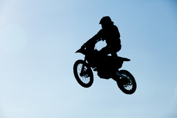 Silhouette of a motocross rider performing a jump on a dirt bike against a clear blue sky