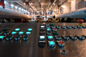 Close-up of a metal control panel with glowing indicator buttons inside an industrial workshop with...