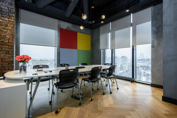 Stylish meeting room with modern furniture, large windows, and colorful wall decor overlooking a cityscape