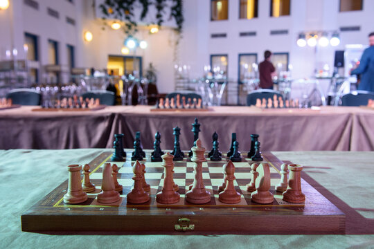 Wooden chessboard with pieces arranged for play in a decorated indoor hall before a chess event or tournament