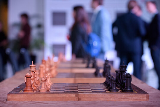 Close-up of a wooden chessboard ready for play with people talking in the blurred background during an indoor event