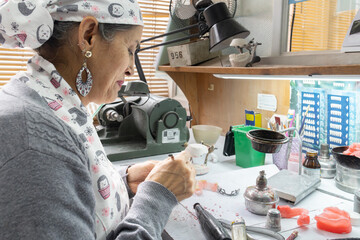 A skilled dental technician adjusts a dental mold with precision tools in a detailed lab setting, showcasing artistry and craftsmanship