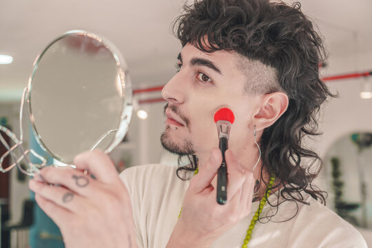 Young man applying makeup while looking in mirror - Powered by Adobe