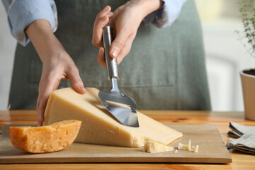 Woman cutting delicious cheese with slicer at wooden table indoors, closeup