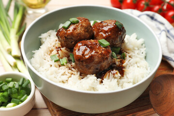 Delicious rice with meatballs, sauce and green onions on white wooden table, closeup