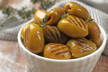 Grilled green olives with thyme in bowl on table, closeup