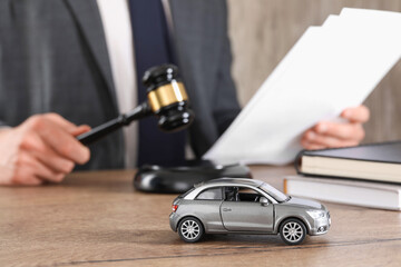 Auto accident law. Man with document and gavel at wooden table indoors, focus on toy car