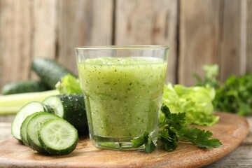 Healthy parsley smoothie in glass, leaves and cucumber on wooden table, closeup
