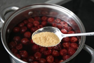 Adding sugar into tasty cherry compot in pot on stove, closeup