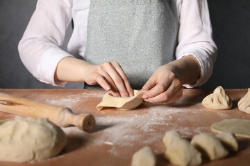 Woman making khinkali on table in kitchen, closeup