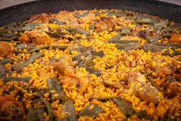 Close‑up of traditional Valencian paella—rabbit, chicken, flat beans and saffron‑coloured rice—simmering outdoors in a wide iron pan during a family cook in eastern Spain.