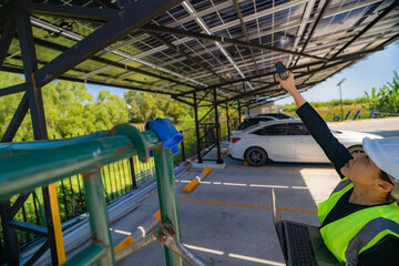 Female engineer inspecting solar panels on a carport while holding a laptop and infrared...