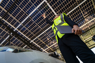 Technician inspects solar panels under a large solar carport structure. Focused on clean energy,...