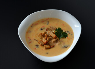 Cheese cream soup with croutons and mushrooms in a deep plate on a black background.