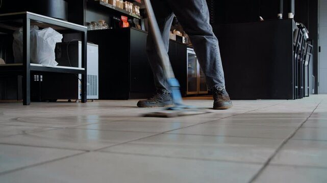 An anonymous barista thoroughly mops the floor after a full day of service in a contemporary cafeteria, ensuring cleanliness and order