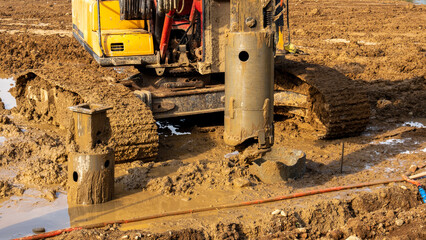 Close-up of drilling machine operating on muddy construction site during foundation work, showing...