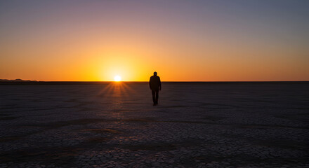 Fototapeta premium Contemplative Stroll Silhouetted Against Dramatic Desert Sunset Setting in the Distance