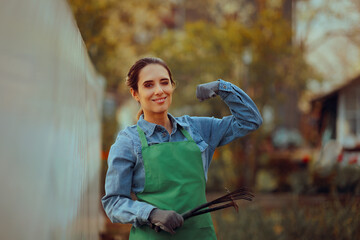 Happy Farmer Flexes Arm Holding Tools in her Hand. Strong woman takes care of her own garden with her own hands 
