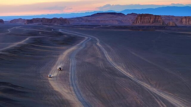 Aerial view of two off road vehicles kicking up dust on desert tracks through yardang formations at dusk