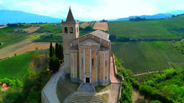 OFFIDA, ITALY - AUGUST 4, 2024: Aerial arcing truck right pan left shot of Chiesa di Santa Maria della Rocca. A cliffside 14th-century marvel with crypt-to-church ascent & frescoed nave