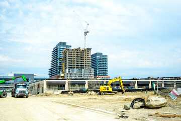 construction site in the city with high rise cranes and a large backhoe doing on going earth work shot in north toronto in spring room for text