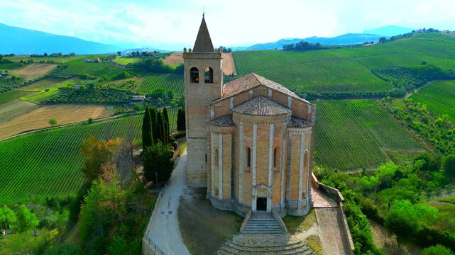 OFFIDA, ITALY - AUGUST 4, 2024: Aerial arcing truck left pan right shot of Chiesa di Santa Maria della Rocca. A Romanesque-Gothic temple standing on a cliff with frescoes attributed to Vincenzo Pagani