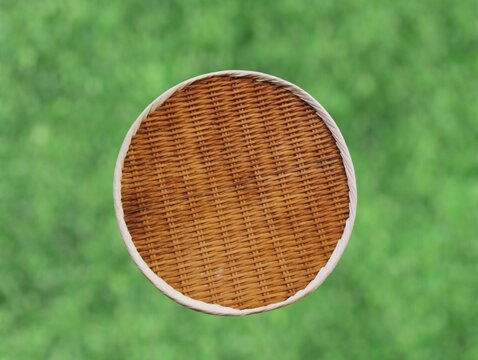 The background of the picture is a blurred image of a green lawn. In the picture is a finely woven bamboo and rattan winnowing basket or tray with a rim and is lightweight and can be used to hold food
