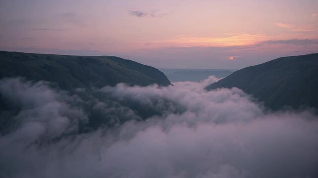 Misty valley at sunset with rolling clouds and distant hills
