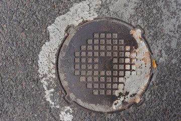 Rusty Manhole Cover On Asphalt Road With Worn And Painted Surface