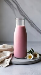 Glass bottle filled with pink smoothie placed on a stone plate with white daisies and beige cloth on a marble background, perfect for healthy lifestyle, diet, and food photography concepts

