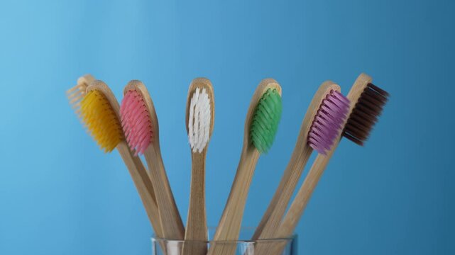 Set of colorful bamboo toothbrushes in glass on blue background, close up, rotates. Zero waste, plastic free, eco friendly organic product concept