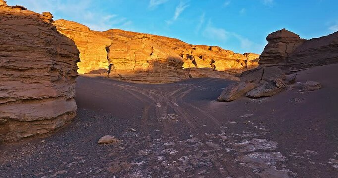 Desert canyon landscape with tire tracks in golden sunlight. Famous yardang landform natural scenery in Xinjiang, China.