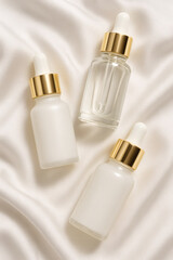 Elegant skincare display featuring dropper bottles with gold accents, set on a soft, white fabric background creating a serene, minimalist aesthetic.