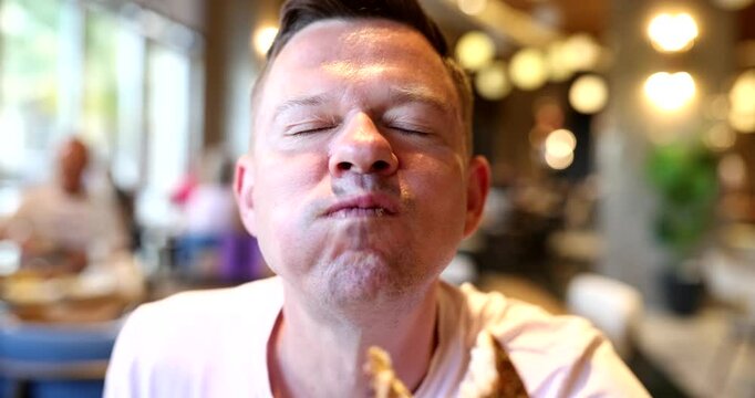 Man bites large piece of fresh bun expressing great pleasure in cozy cafe. Male guest eats tasty handmade pastry visiting local bakery for lunch