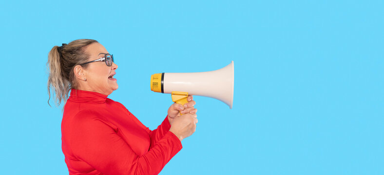 Woman enthusiastically speaking into a megaphone against a bright blue background while wearing stylish glasses