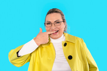 Brightly dressed woman joyfully pointing to teeth with playful smile against a vibrant blue...