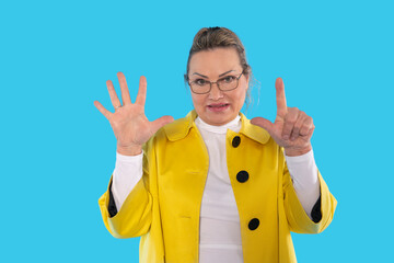 Woman in bright yellow coat playfully showing seven fingers against a blue background in a creative...