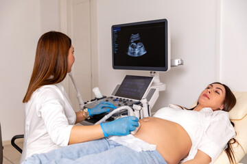 The pregnant woman is lying down in a hospital, doctor using ultrasound equipment screening of...