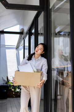 Business woman with box cardboard packing personal items after losing jobs. asian business woman standing on office background. Your fired Unemployed Jobless People Crisis
