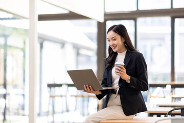 Portrait of asian businesswoman standing holding and using a laptop in the office. independent creative design business.
