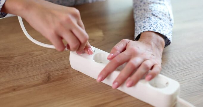 Woman office worker inserts white plug into electrical extension cord. Businesswoman sits at table and connects lamp by pushing plug into outlet
