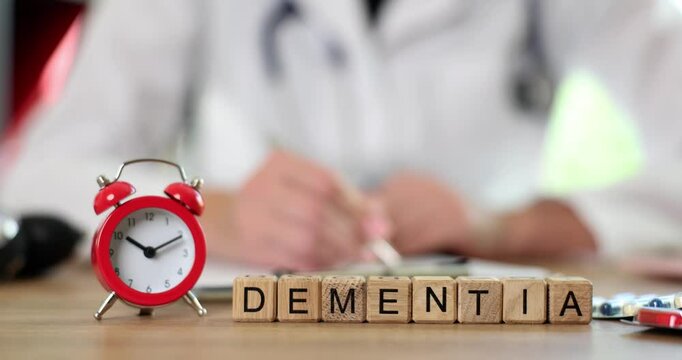Miniature wooden blocks on hospital table form word DEMENTIA near alarm clock. Physician writes stages of treatment process in notebook. Slow motion