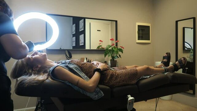 n a neatly arranged studio, the client lies stretched out on a treatment bed while the esthetician works under a bright ring light. The calm setup emphasizes precision and care in real time.