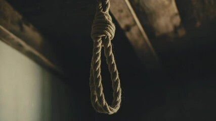 Rope noose hanging indoors against dark background in dimly lit room with a wooden ceiling adding to somber mood, concept.