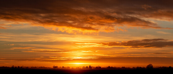 Fototapeta premium Golden sunrise illuminates sky with vibrant clouds over serene landscape