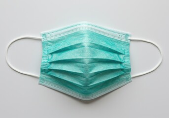 A single light green surgical mask with white ear loops laying on a plain white surface in a studio shot