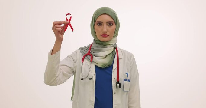 Doctor in hijab holds red ribbon and colorful condom packets in hands. Woman presents information about AIDS awareness and safe sex practices