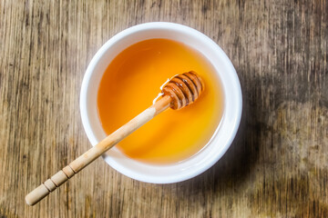 honey in a bowl with a honey dipper on wooden table