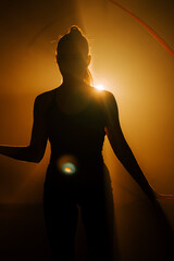Woman performs rhythmic gymnastics under dramatic lighting in a flat space