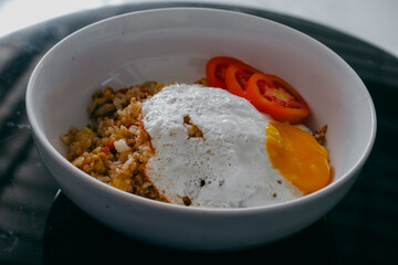 Delicious spicy village-style fried rice served in a white bowl, topped with a sunny side up egg and accompanied by sliced fresh tomatoes.